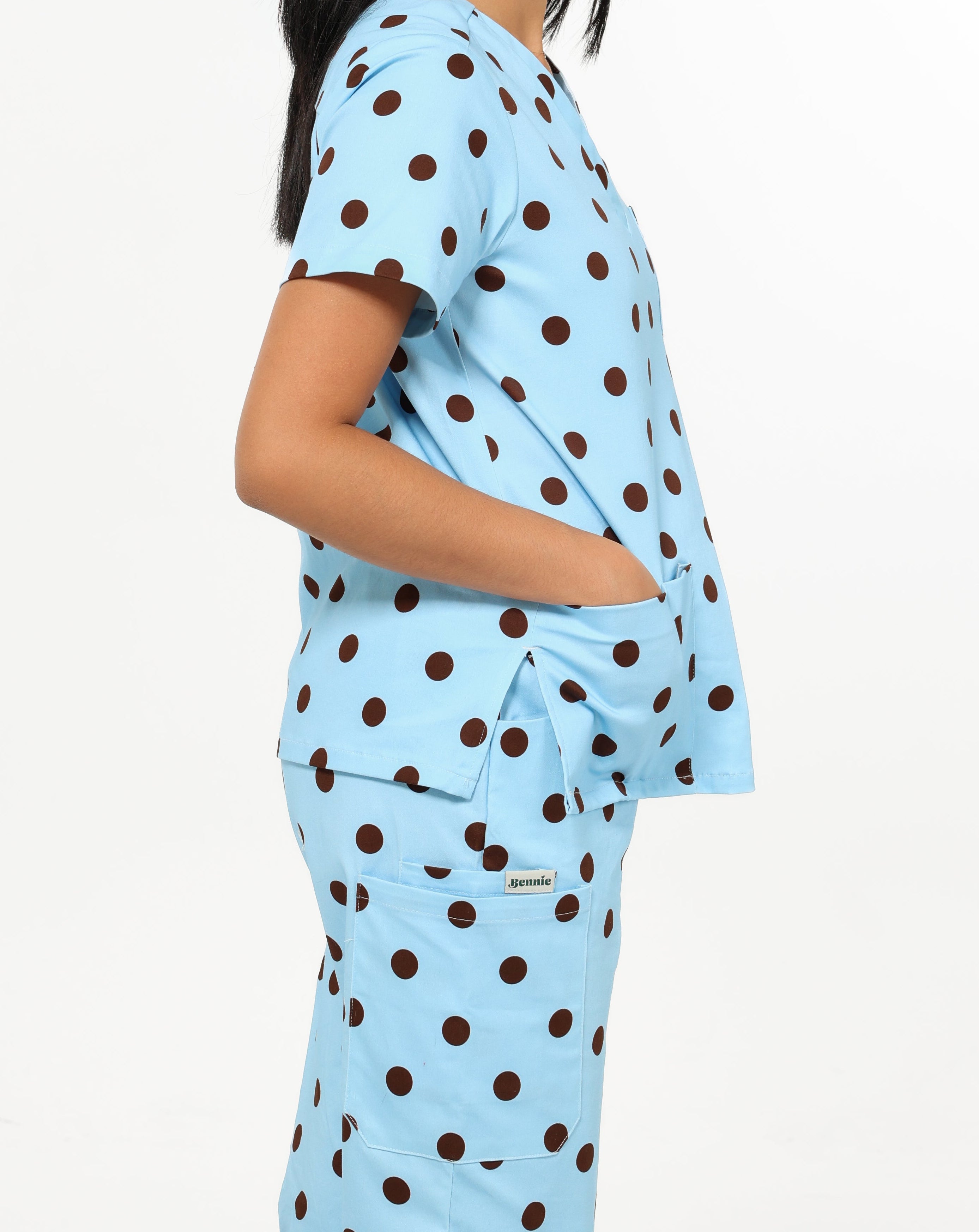 Person wearing a light blue scrub set with brown polka dots on a white background