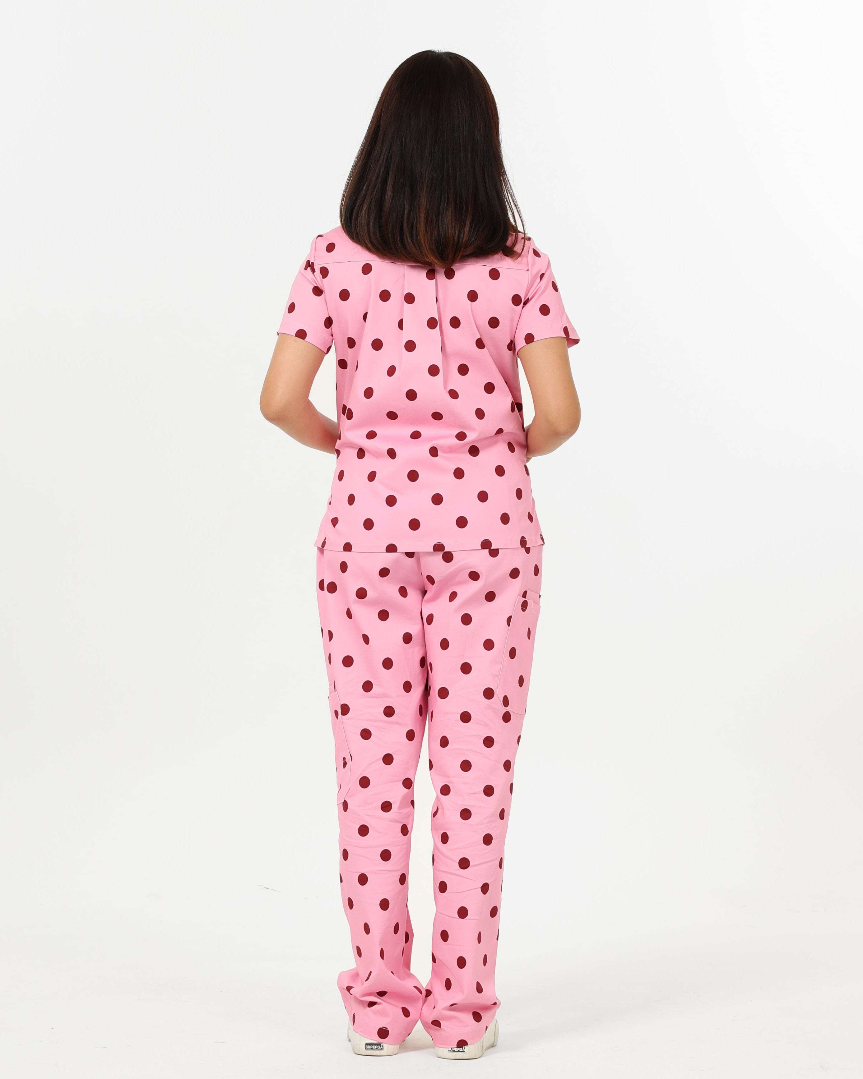 Person wearing pink polka dot scrub set on a white background