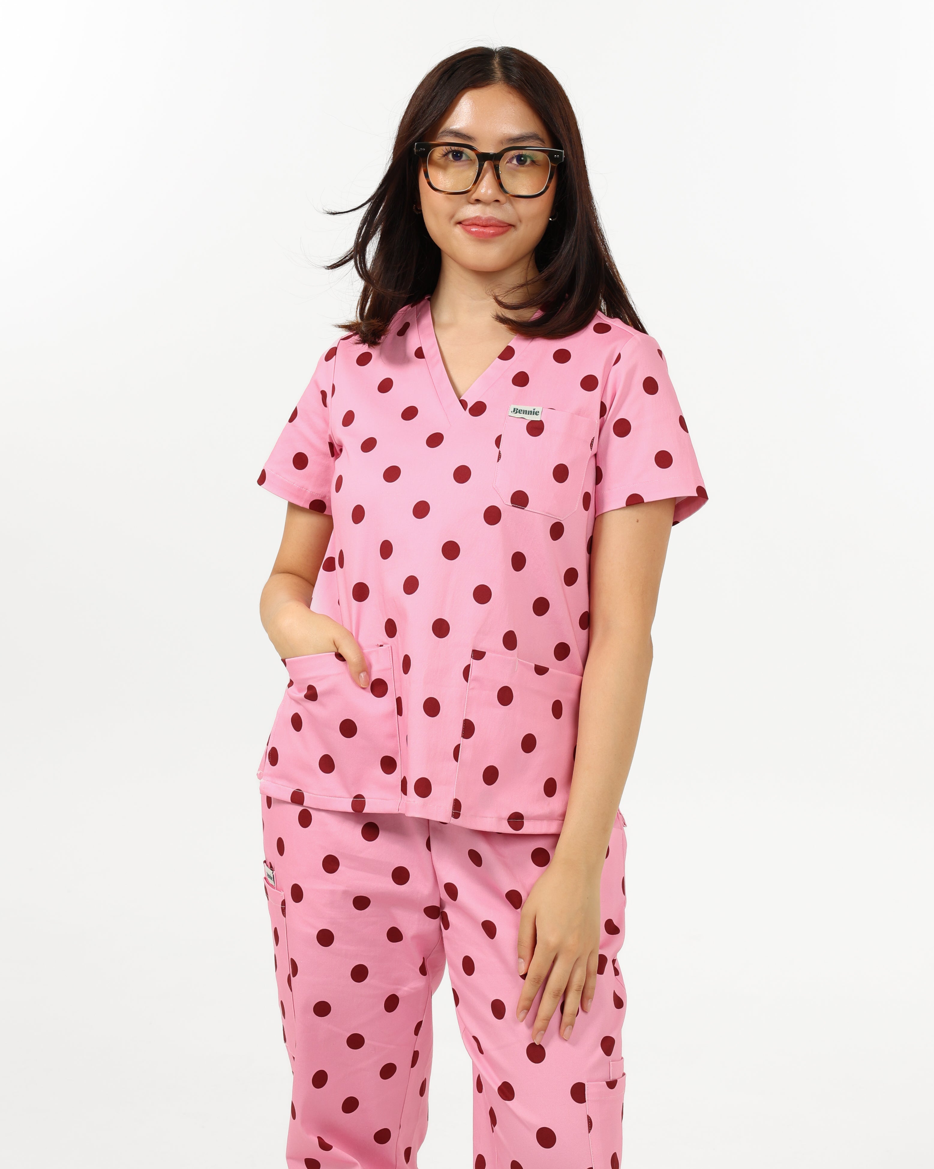 Person wearing pink polka dot scrub set on a white background