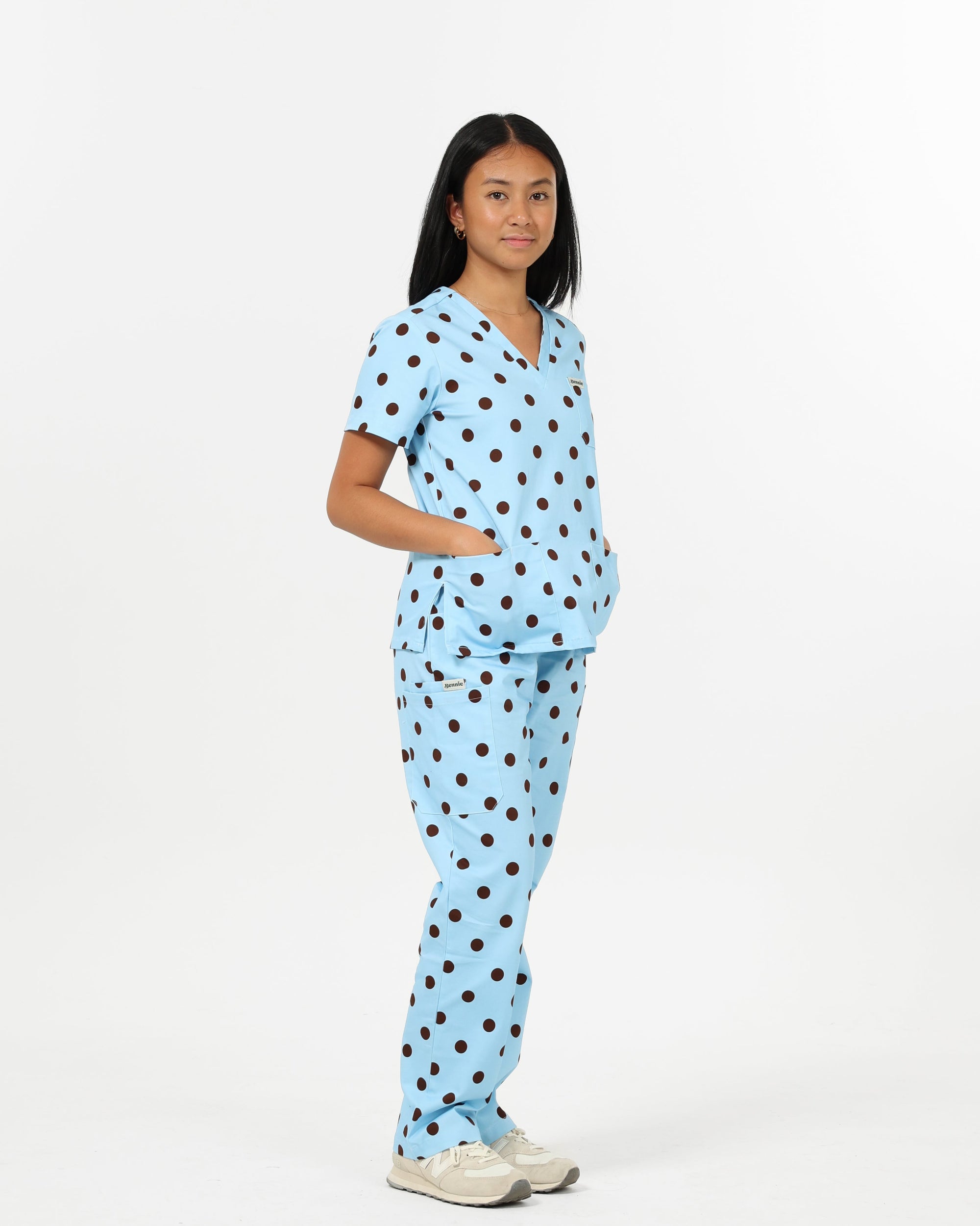 Person wearing a light blue scrub set with brown polka dots on a white background