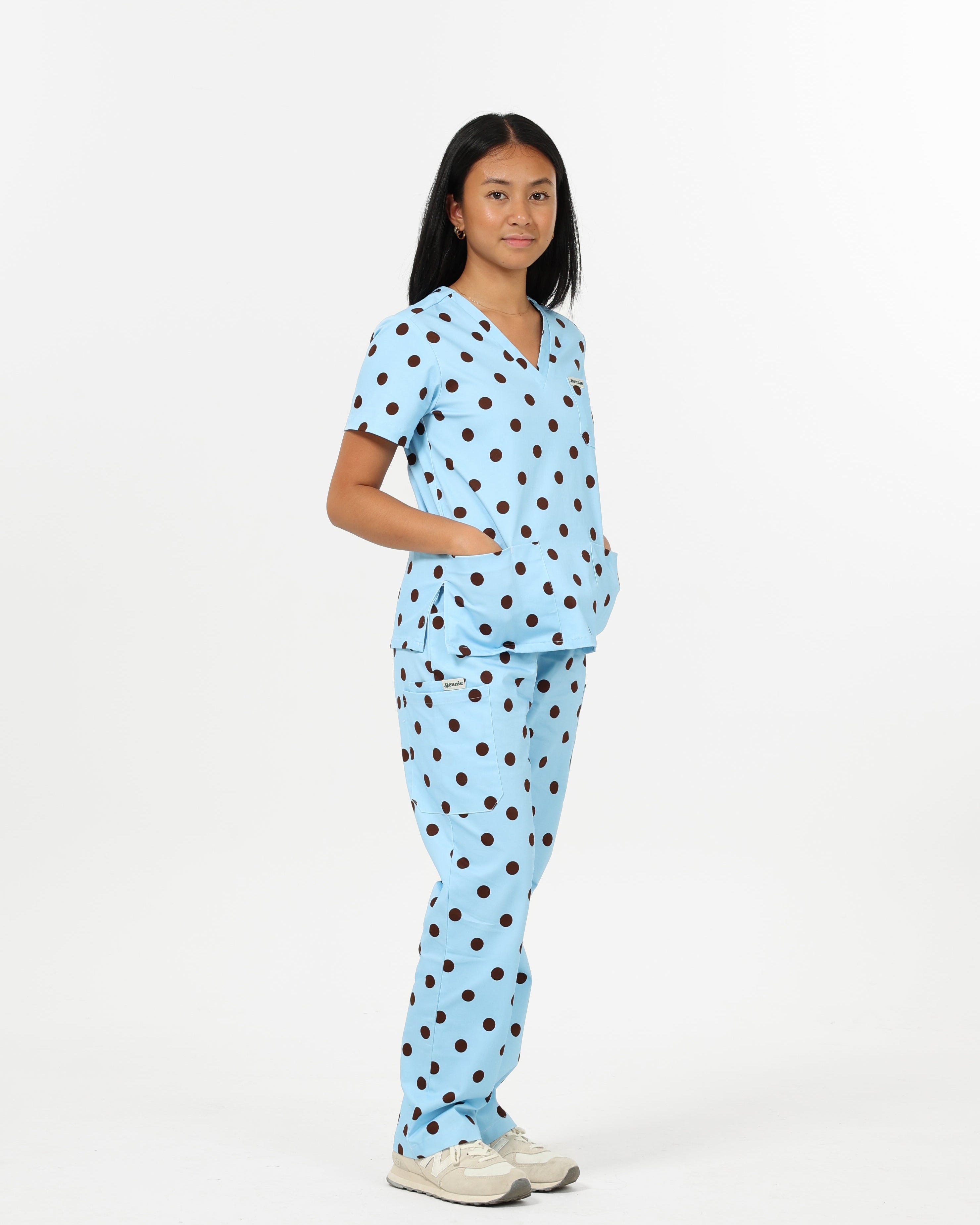 Person wearing a light blue scrub set with brown polka dots on a white background