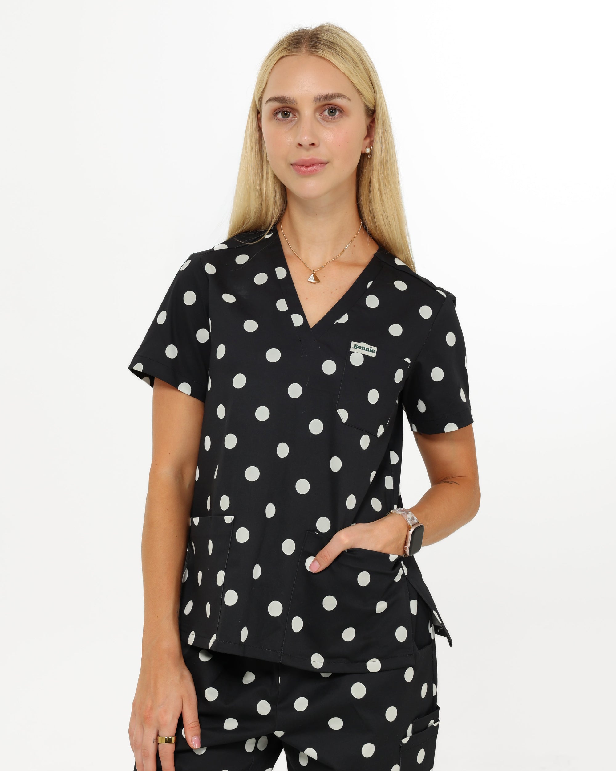 Woman wearing a black polka dot scrub top and pants on a white background