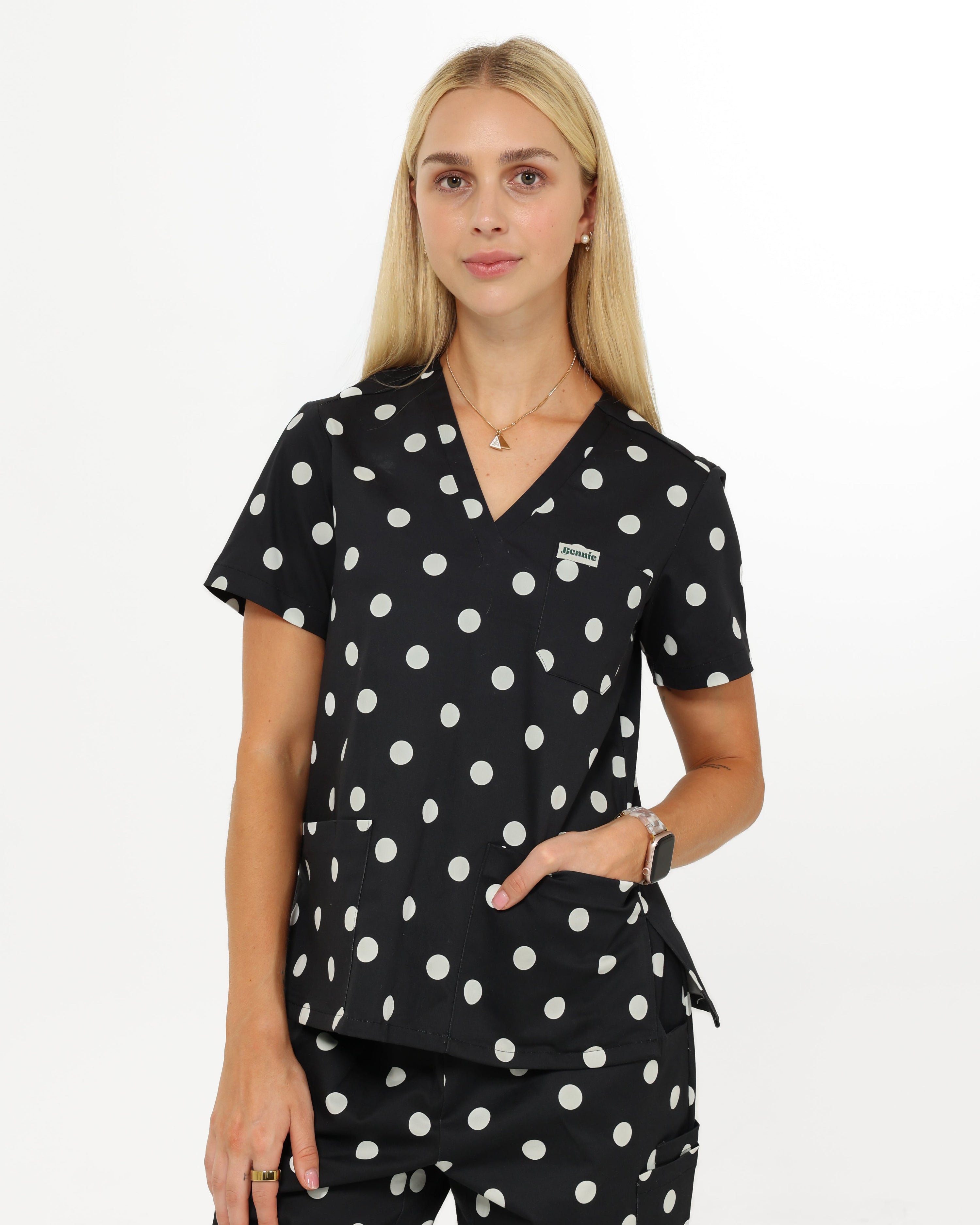 Woman wearing a black polka dot scrub top and pants on a white background
