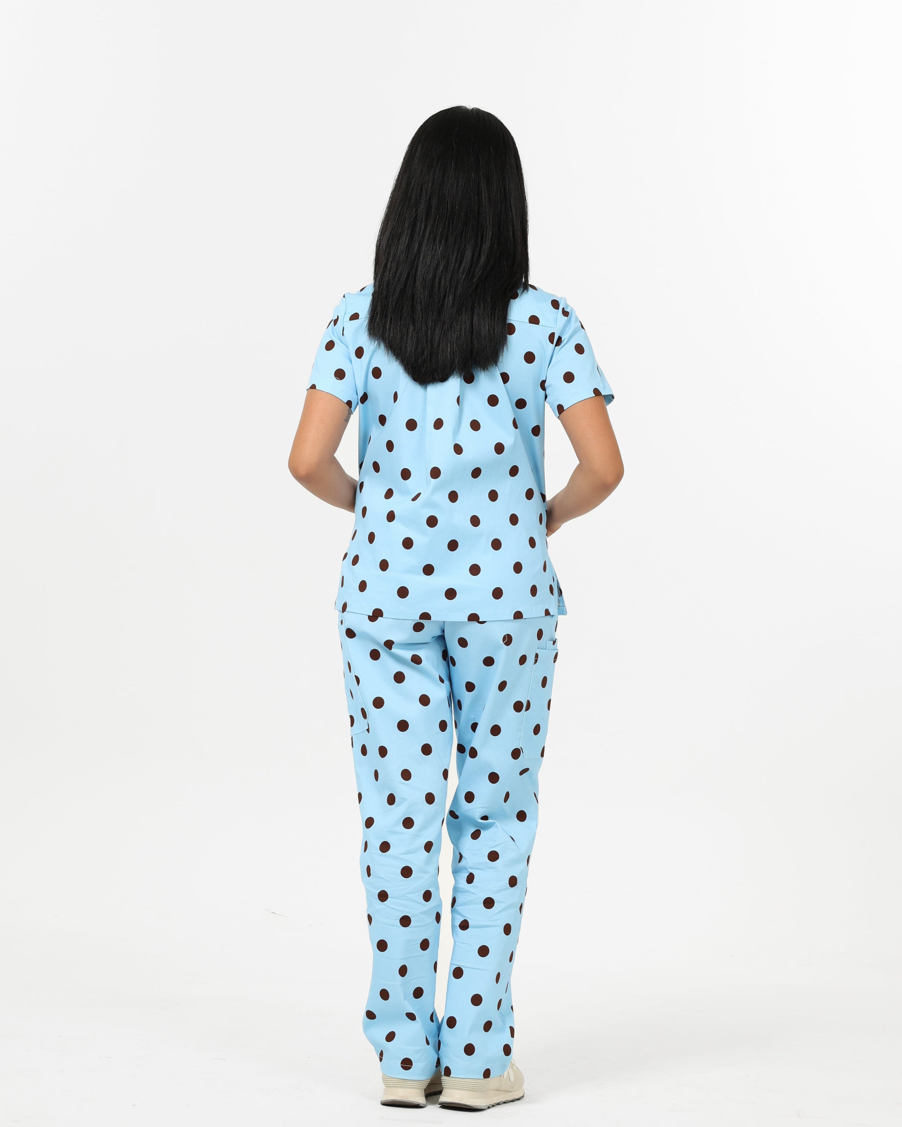 Person wearing a light blue scrub set with brown polka dots on a white background