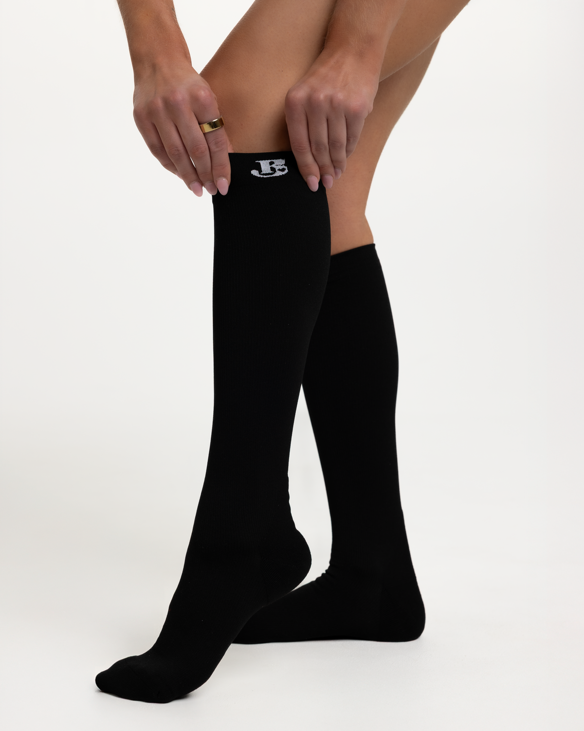 A person wearing black knee-high compression socks, with one sock being adjusted at the top. The white logo on the top cuff.
