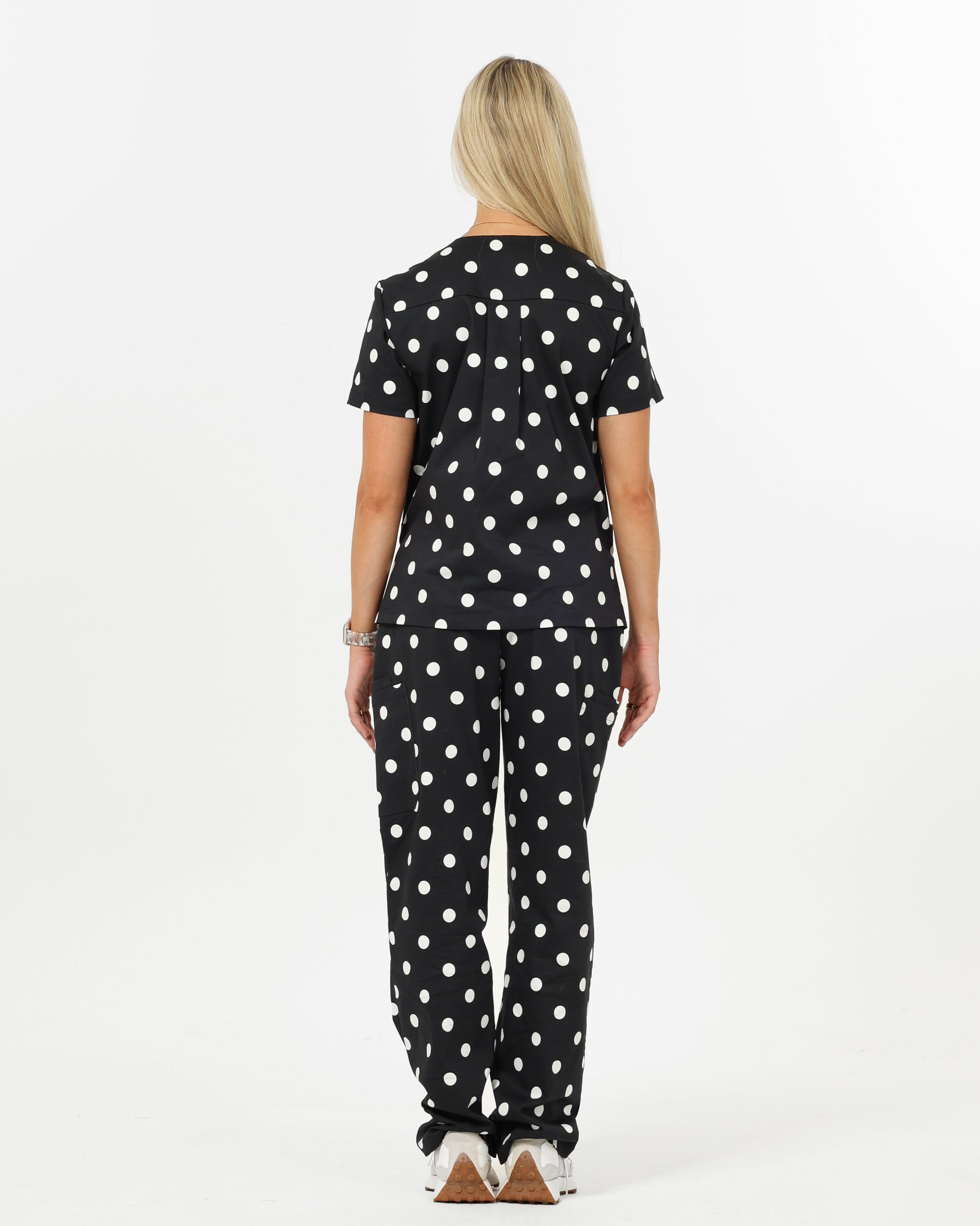Woman wearing a black polka dot scrub set on a white background