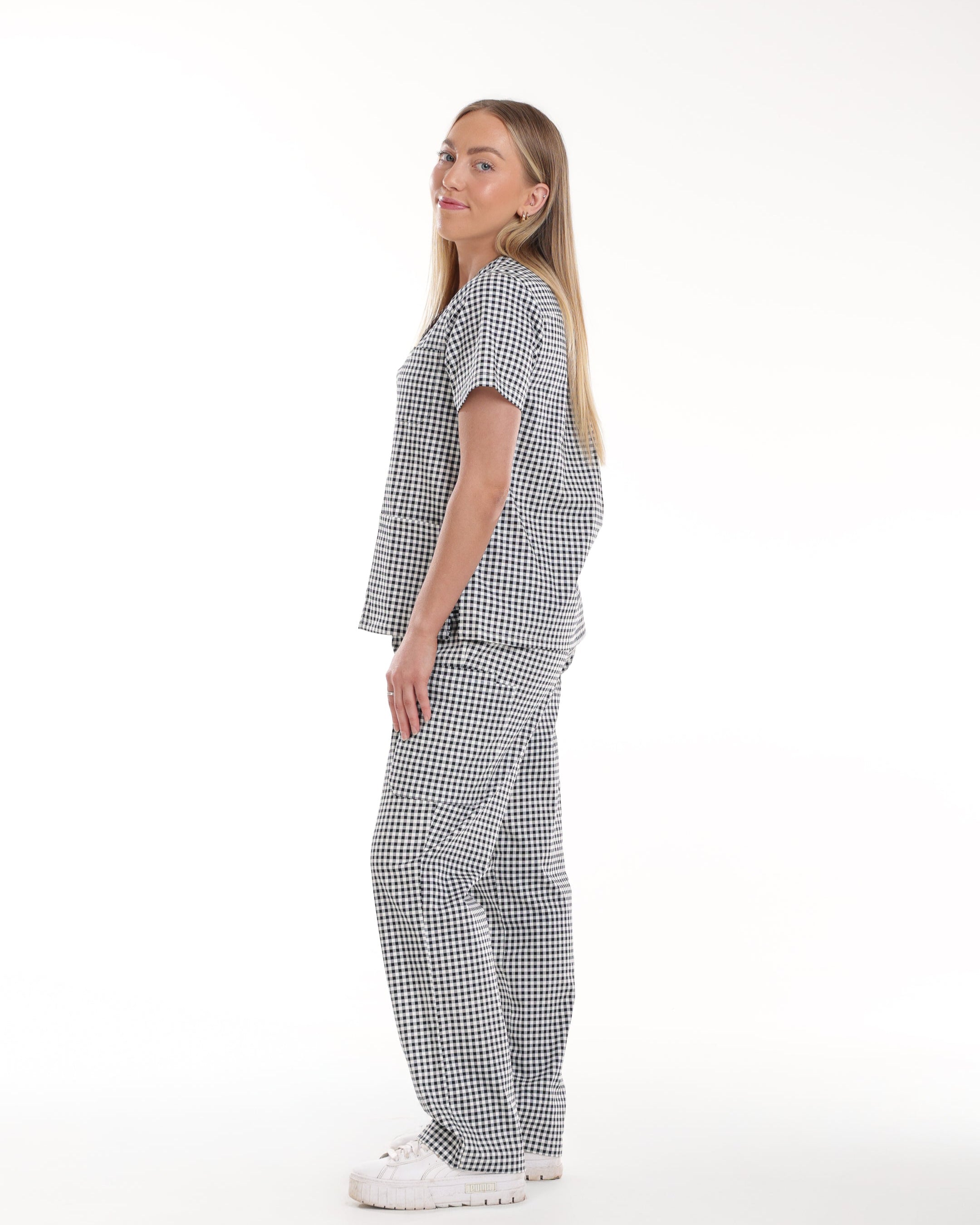 Side full body view of Model wearing Bennie Frankie Scrub Set in black and white gingham print, showcasing full outfit with short sleet top and straight-leg pants 