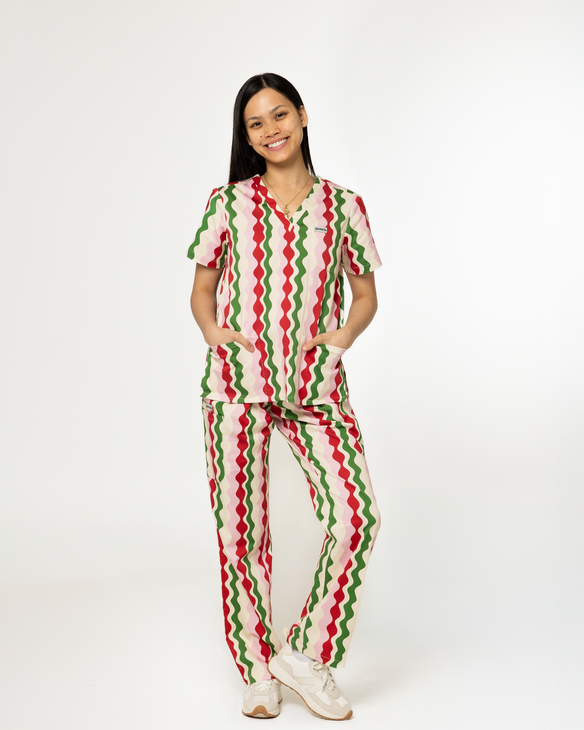 A woman modeling a matching scrub set with a red, green, and cream zigzag pattern, standing against a plain white studio background.