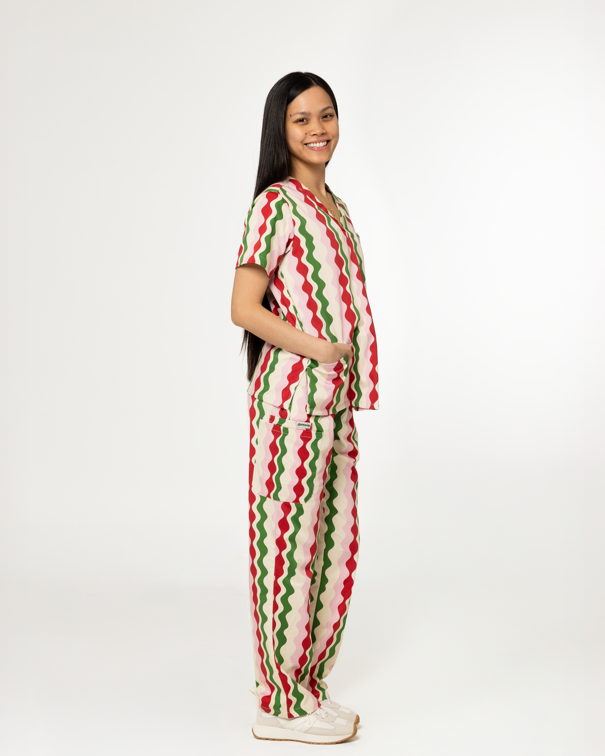 A woman modeling a matching scrub set with a red, green, and white wavy zigzag pattern, standing against a plain white studio background.