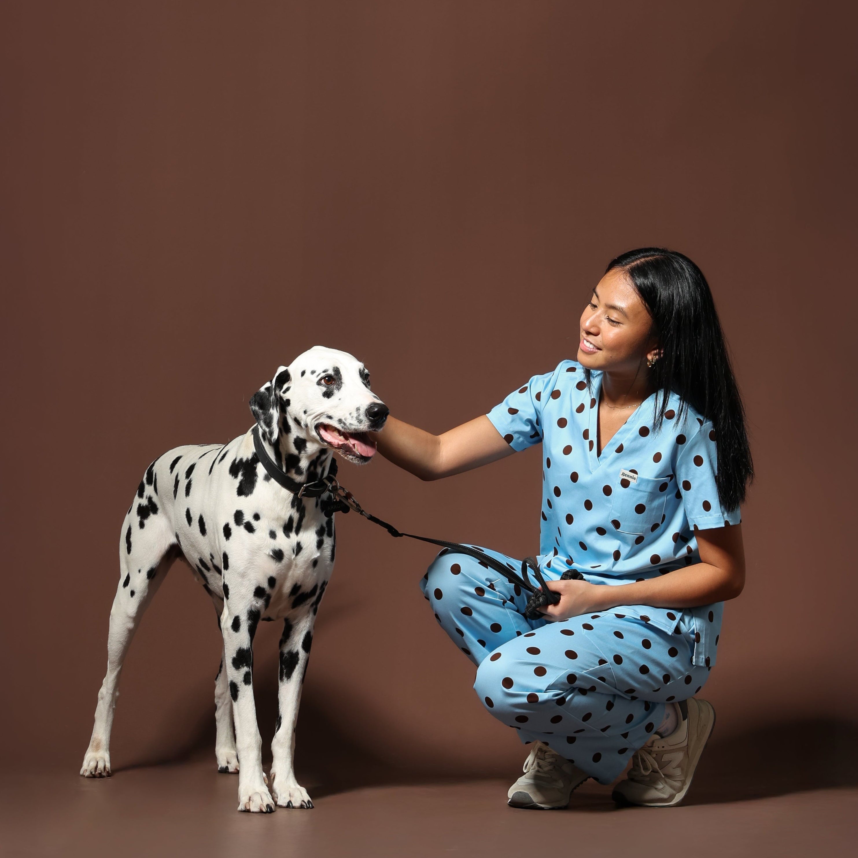 Woman in matching blue polka dot scrubs with a Dalmatian dog on a brown background